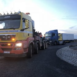 Ciężka laweta przygotowująca się do pomocy unieruchomionej na poboczu ciężarówki o zmierzchu we Wrocławiu.