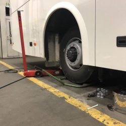Autobus w trakcie konserwacji ze zdemontowanym kołem, wspartym na podnośniku hydraulicznym, w warsztacie serwisowym.