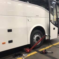 Autobus Volvo w trakcie konserwacji lub wymiany opon w warsztacie serwisowym w Trzebnicy, z podnośnikiem hydraulicznym i narzędziami rozłożonymi na podłodze.
