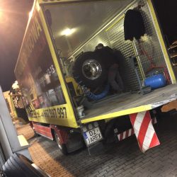 Widzi się osobę pracującą nocą z tyłu kolorowej ciężarówki serwisowej w Trzebnicy, wokół niej widać różne urządzenia i węże.