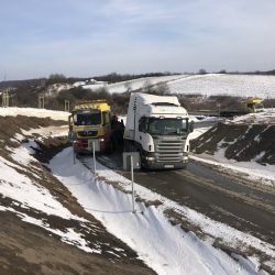 Ciężarówki budowlane poruszają się po błotnistym terenie po częściowo zaśnieżonej drodze pod Wrocławiem.