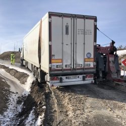 Ciężarówka utknęła na poboczu drogi pod Wrocławiem, a w pobliżu laweta, co sugeruje, że trwa akcja ratownicza. Śnieg i kępy trawy wskazują, że jest zimno.