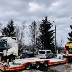 Ciężka laweta przewożąca uszkodzoną naczepę i zbiór innych pojazdów, prawdopodobnie biorących udział w wypadku lub transportowanych do naprawy, pod zachmurzonym niebem we Wrocławiu.