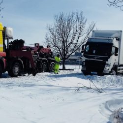 Laweta przygotowuje się do pomocy półciężarówce, która utknęła w śniegu na poboczu drogi.