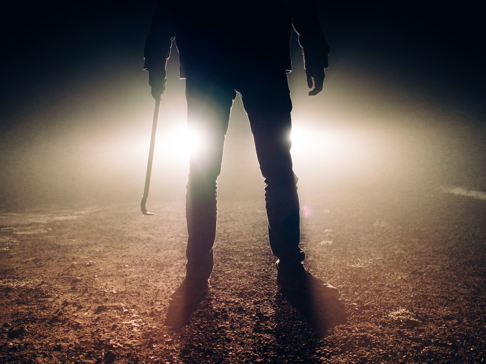 Sylwetka osoby stojącej w mglistej ciemności trzymającej łom, z dramatycznym podświetleniem rzucającym tajemniczy blask